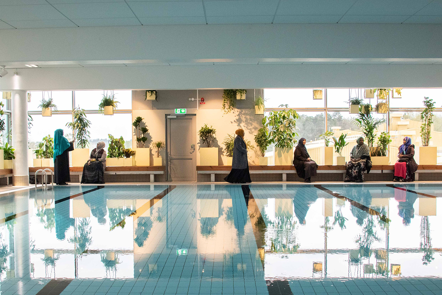 An indoor swimming pool with several women in the background and green plants.