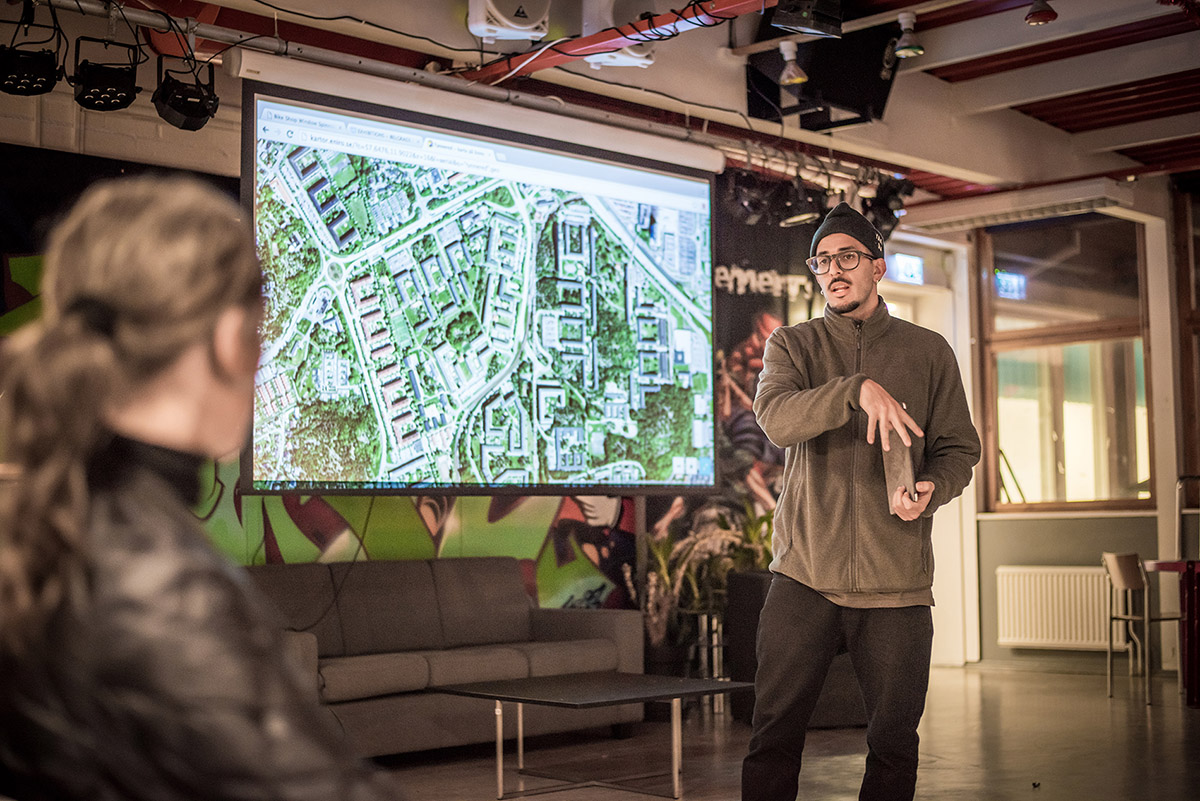 En man står och pratar framför en områdeskarta på en projektortavla.