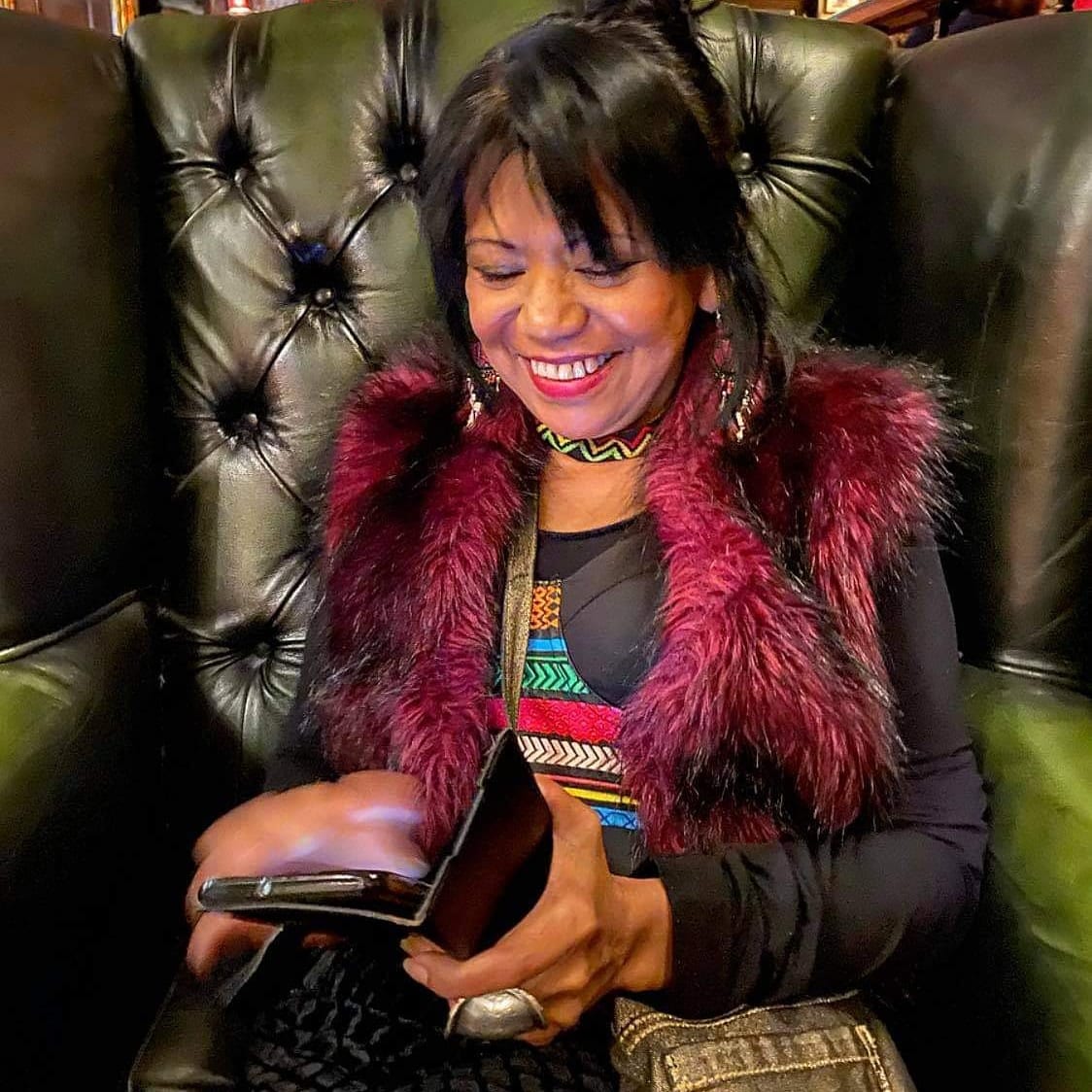 En kvinna sitter i en skinnfåtölj och tittar i sin mobiltelefon. 