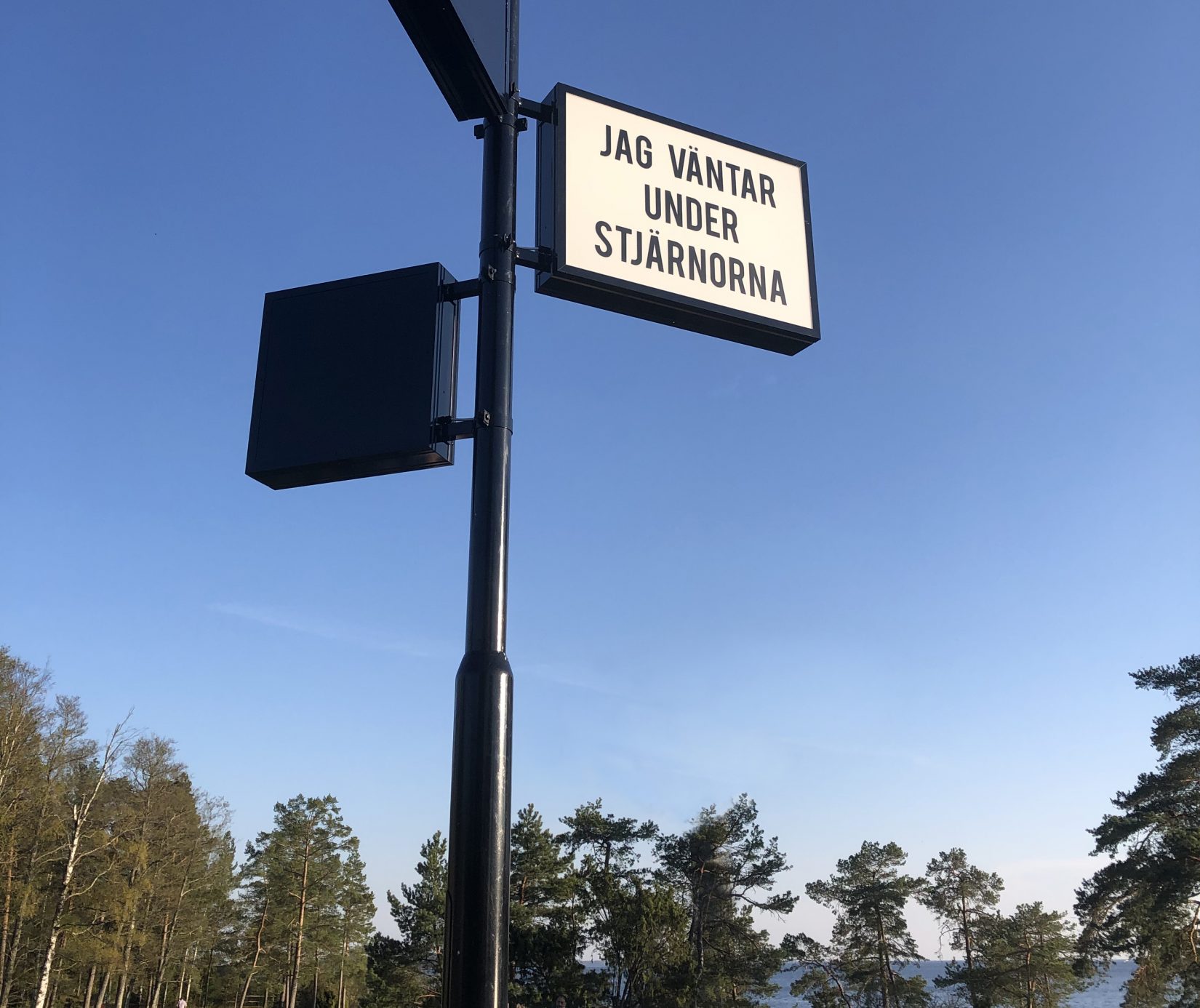 Ljusskylt ses mot blå himmel. På skylten står Jag väntar under stjärnorna.