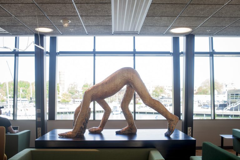 Framför ett fönster står en träskulptur som visar en person som står på händer och fötter.