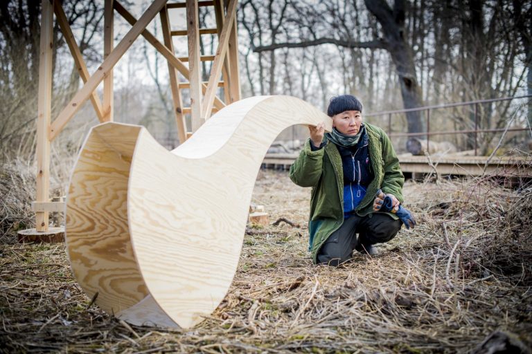 Konstnären håller en stor lur i plywood mot örat