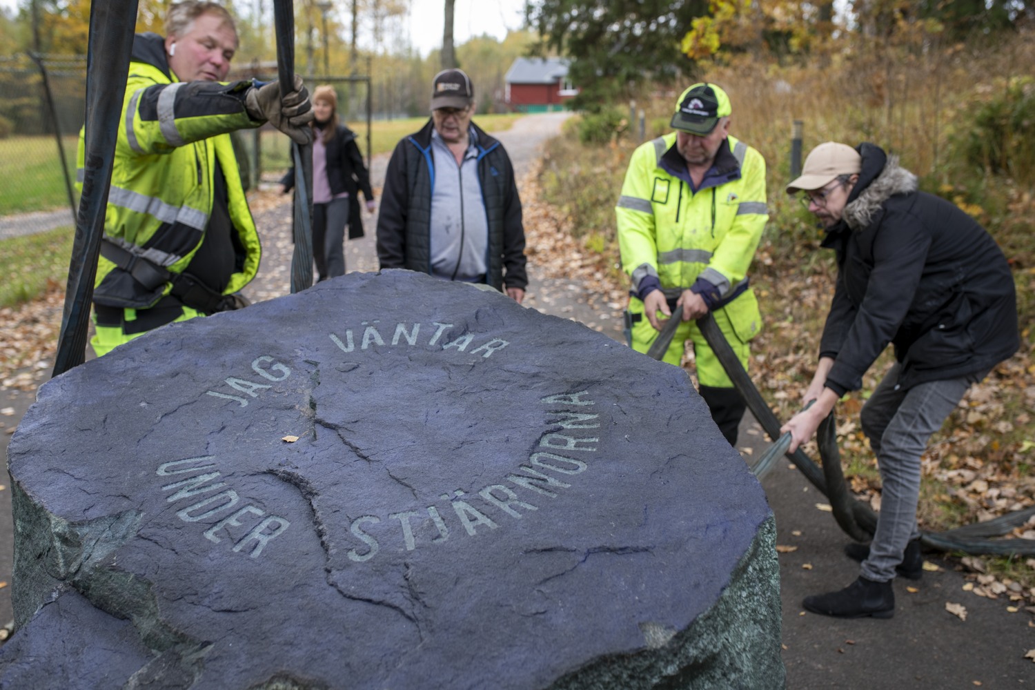 Flera män placerar en stor sten. En sten med graverad text, Jag väntar under stjärnorna