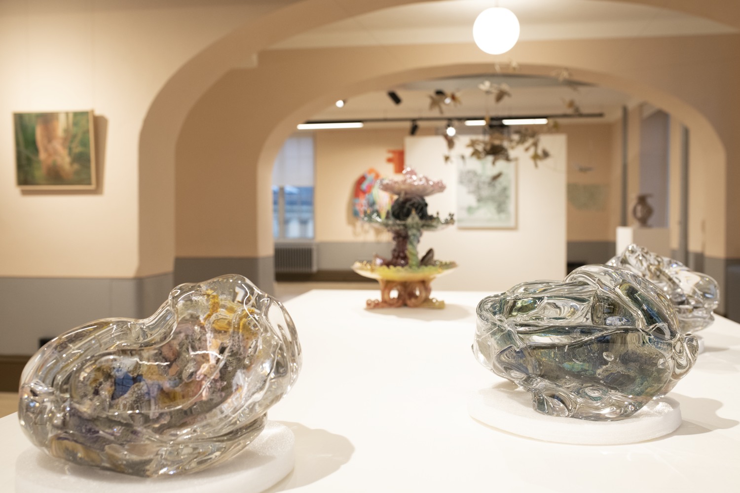 Rumsbild på upphängda tavlor och tre verk på ett bord